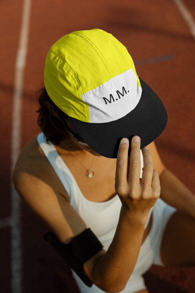 Close-up of person in athletic wear adjusting a yellow and white cap labeled MM on a sports track. Ideal for mockups and digital designs.