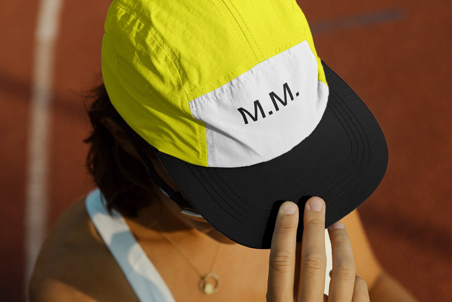 Close-up of a person wearing a yellow and black cap with M.M. text on a sports track. Ideal for mockup design and branding projects for designers.