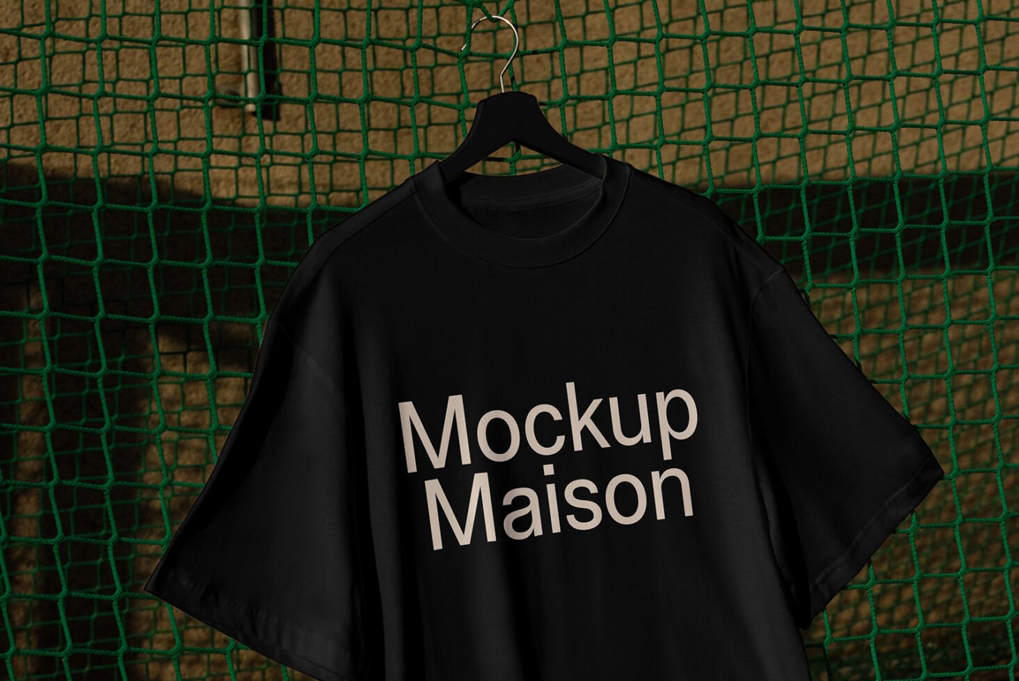 Black t-shirt mockup hanging on a hook with text Mockup Maison displayed against a green net background perfect for designers fashion apparel templates