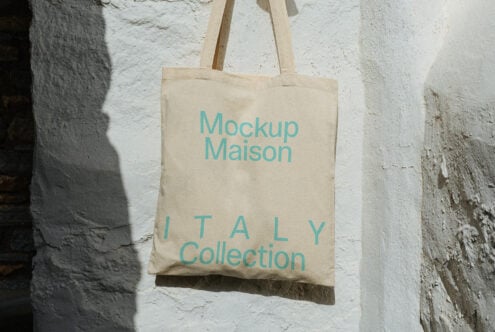 Beige cotton tote bag with turquoise lettering on weathered concrete