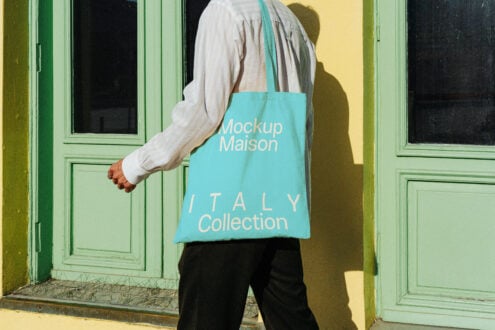 Person holding tote bag with Italy collection text mockup in bright teal. Ideal for fashion branding and product showcase. Outdoor setting.