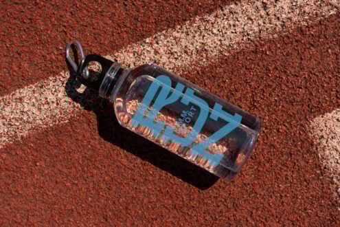 Clear water bottle mockup with blue text on a red athletic track featuring a white line. Ideal for showcasing custom branding and design templates.