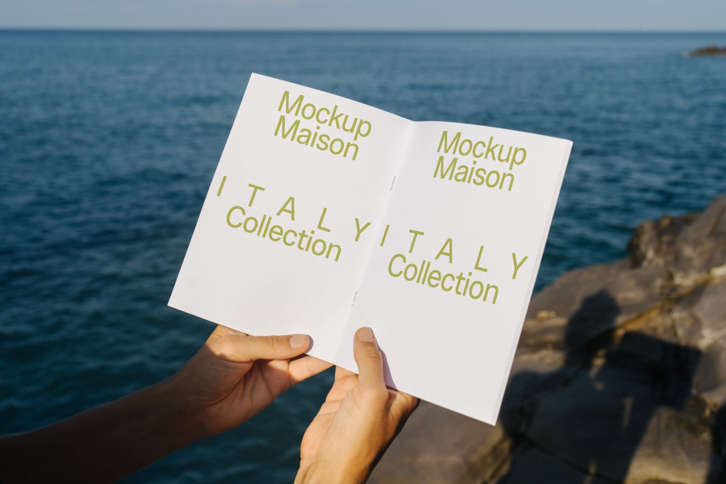 Open booklet mockup featuring modern font design from Italy Collection held by hands with ocean view background ideal for designers and graphic assets.