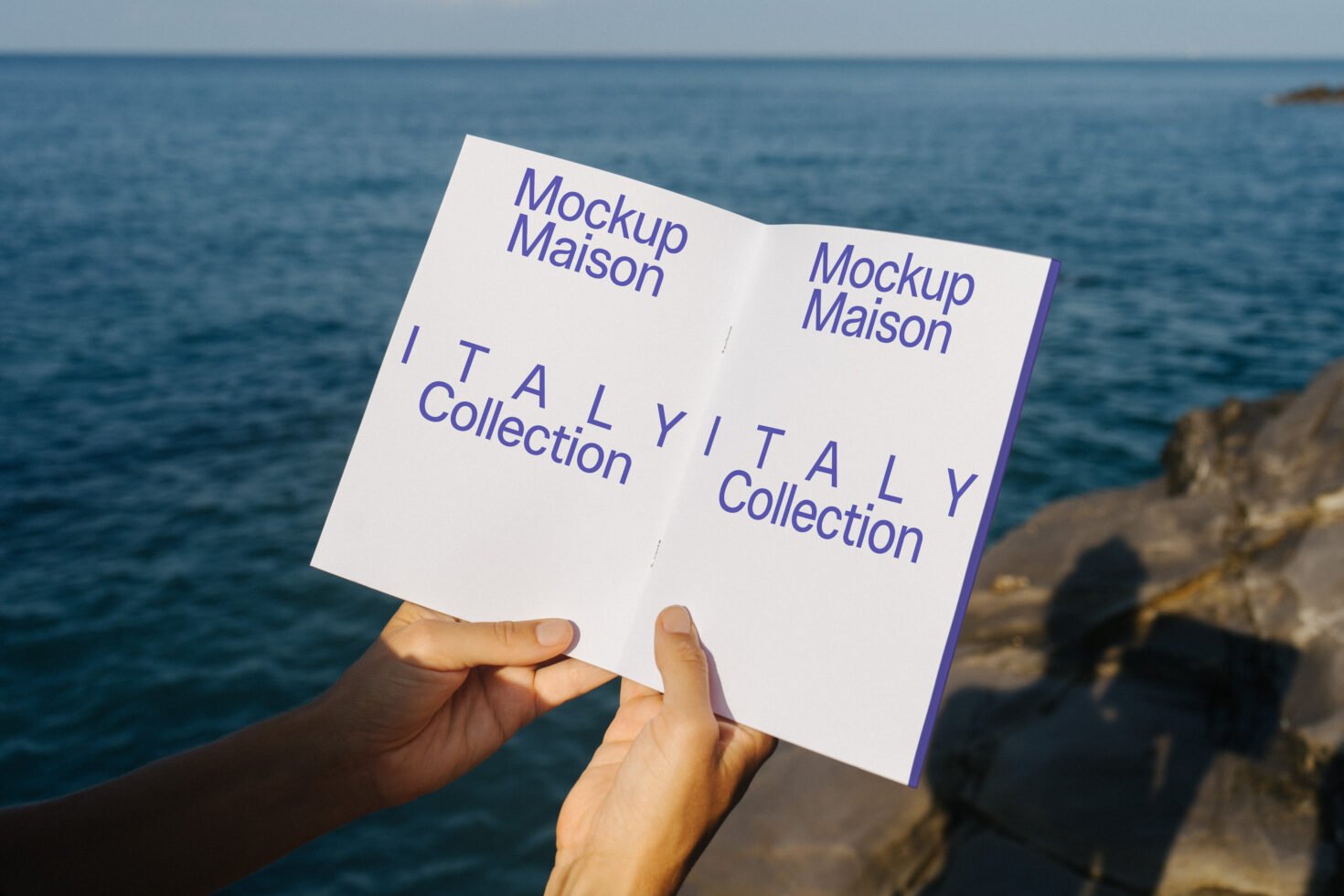 Person holding open brochure mockup labeled Italy Collection over the sea. Ideal for designers, showcasing templates and graphics in a realistic setting.