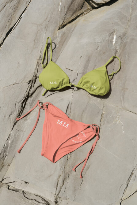 Lime green bikini top, coral bikini bottom with branding on stone surface