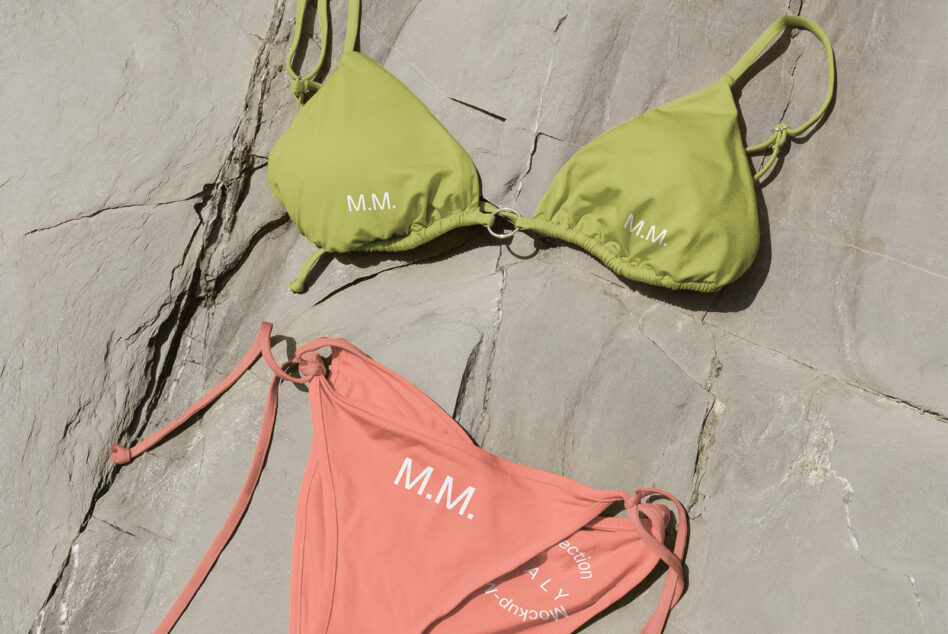 Lime green bikini top with M.M. branding next to coral triangle bottoms on concrete