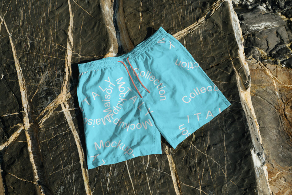 Turquoise swim shorts laid flat on weathered wood with repeat text print
