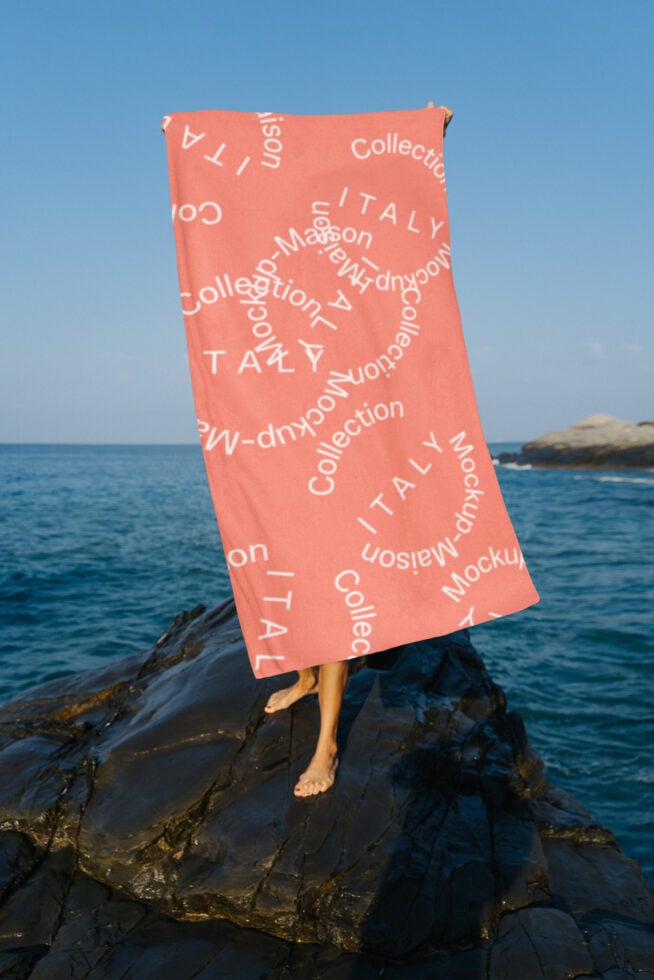 Person holding coral towel with Italy mockup print by the ocean, ideal for designers seeking beach-themed graphics or texture templates, summer feel.
