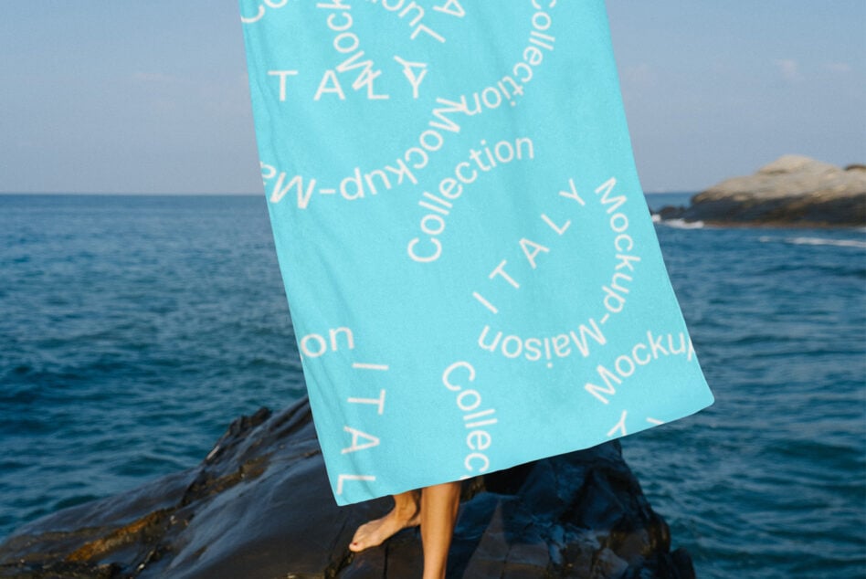 Turquoise towel with scattered white lettering held by person on ocean rocks