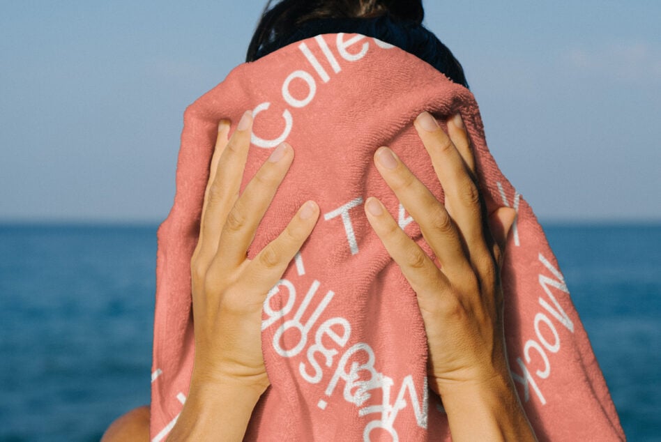 Coral towel with white text held by hands at beach with ocean backdrop