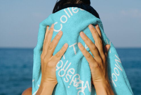 Person holding a turquoise towel covers face with sea background ideal for mockup photography summer template or beach design projects vibrant colors