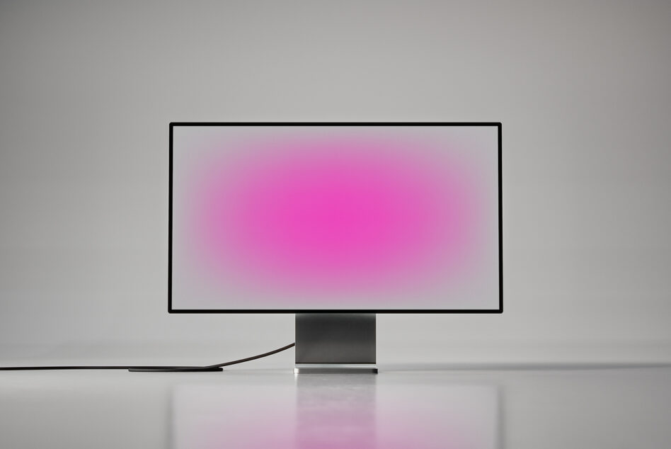 Desktop monitor with pink gradient display on gray pedestal stand