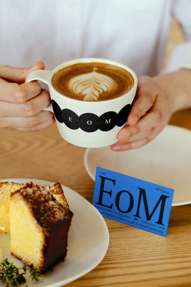 Coffee cup mockup held by hands near cake with styled business card on wooden table. Ideal for graphic design, branding, template creation, and marketing.