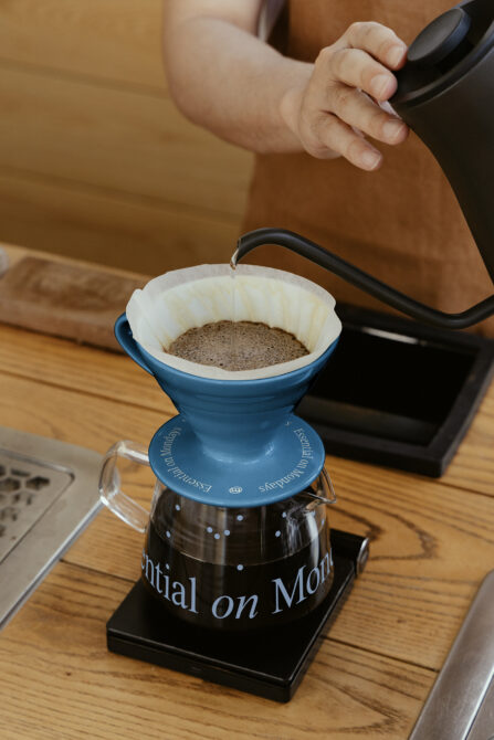 Blue pour over coffee dripper with white filter filled with grounds, black kettle pouring water
