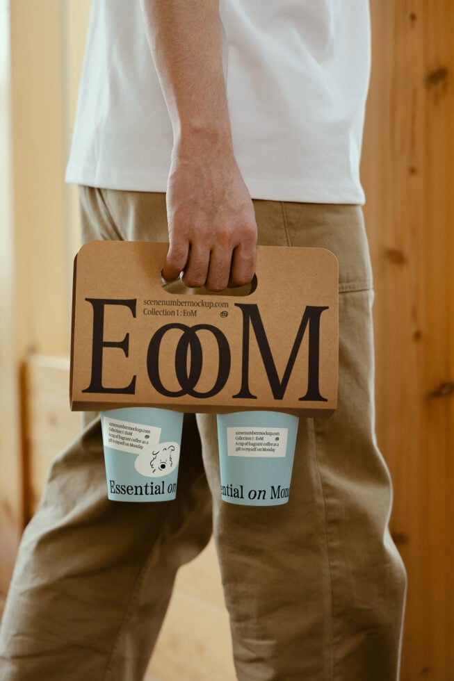 Mockup featuring a person holding a carrier with two coffee cups labeled Essential on Monday. Ideal for branding and packaging design projects.