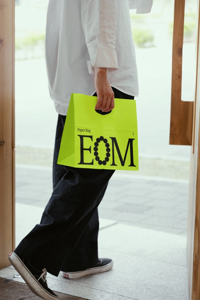 Person carrying a stylish neon green paper bag with typography design exiting a store. Ideal for mockups graphics branding templates for designers.