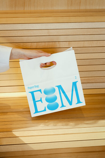 White paper bag mockup with blue E8M text on wooden floor backdrop