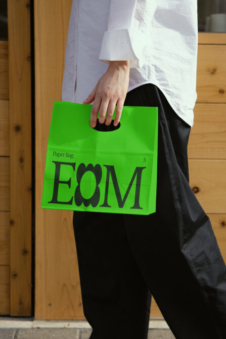Woman carrying bright green paper bag with black E8M lettering outdoors