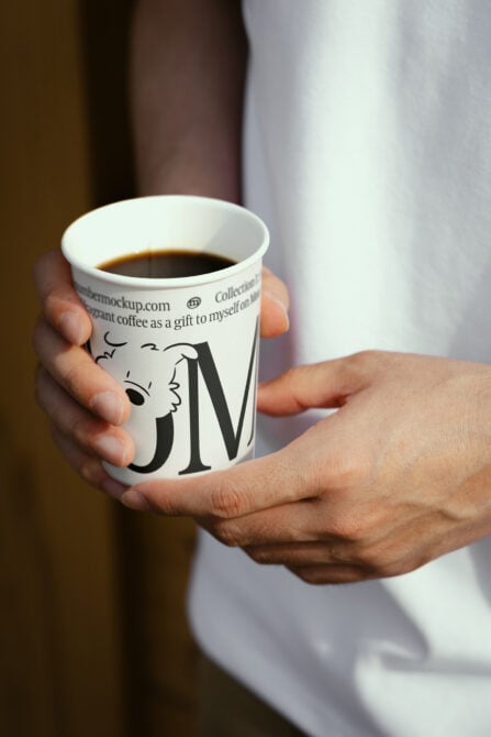 Close up of hands holding white paper coffee cup with sketch illustration