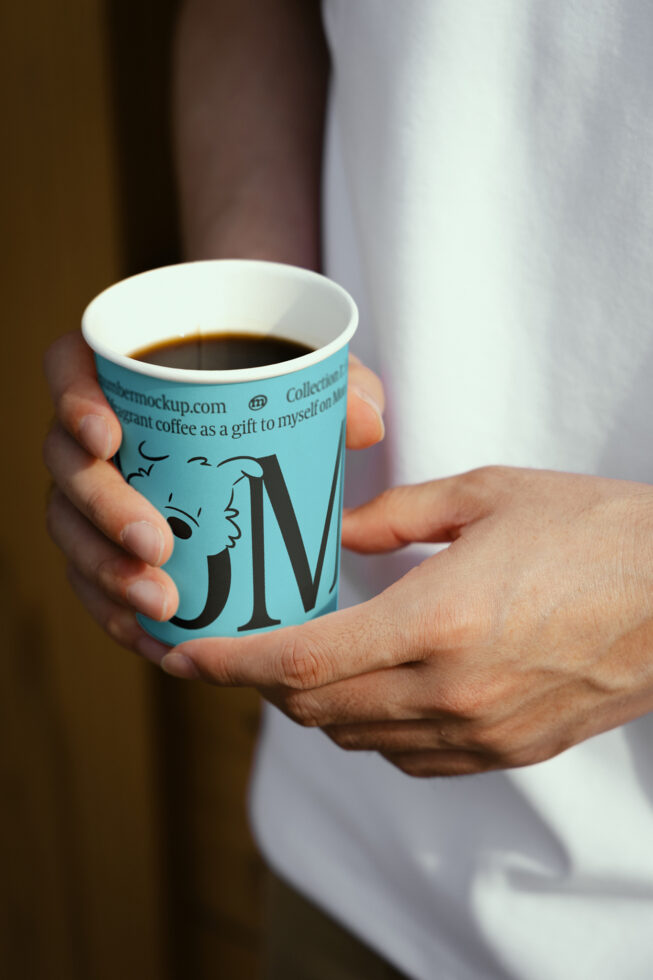 Close-up of a hand holding a coffee cup featuring custom graphic design. Perfect for designers seeking creative mockups or print templates for branding.