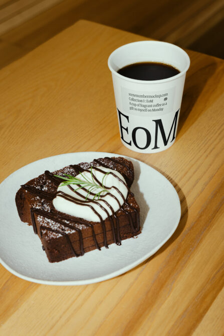 Chocolate cake slice with whipped cream on white plate next to coffee cup