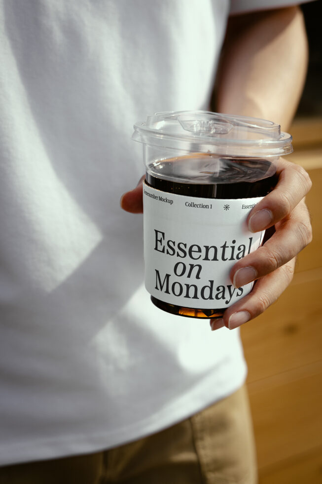 Person holding a takeaway coffee cup with custom sleeve reading Essential on Mondays. Ideal for product mockup or branding design showcasing template.