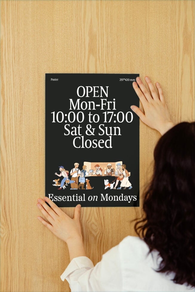 Person hangs a business hours poster on a wooden wall featuring diverse cartoon characters, ideal for designer mockups and graphic templates.