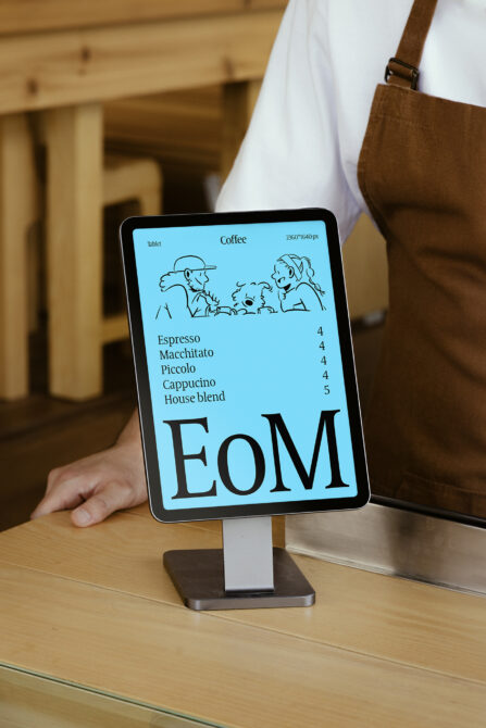 Tablet mockup displaying EoM coffee menu with blue background, line illustrations, drink prices