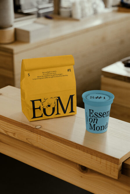 Golden yellow paper bag beside light blue coffee cup with matching EoM branding displayed