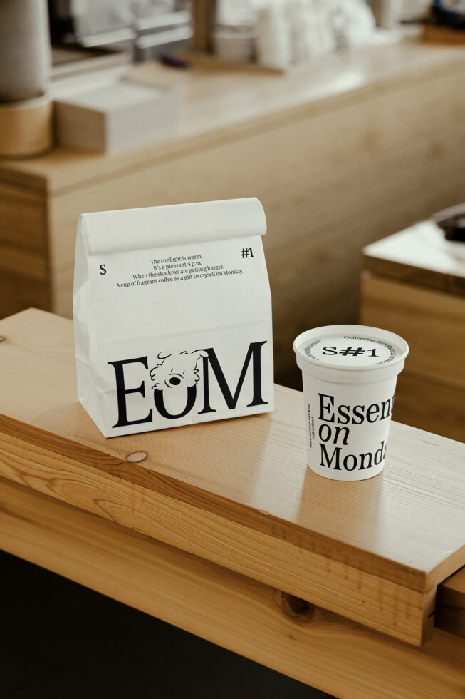 Coffee shop branding mockup featuring a paper bag and cup on a wooden counter. Modern typography with EOM logo design. Ideal for packaging template.