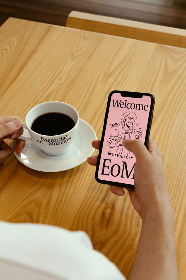 Designer holding smartphone with playful graphic design mockup Welcome to EoM and coffee cup on table. SEO keywords mockup design graphic smartphone