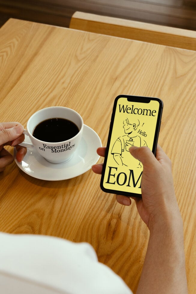 Person holds smartphone showing greeting, beside coffee cup on wooden table suitable for design mockup. Keywords: mockup, design, smartphone, coffee.