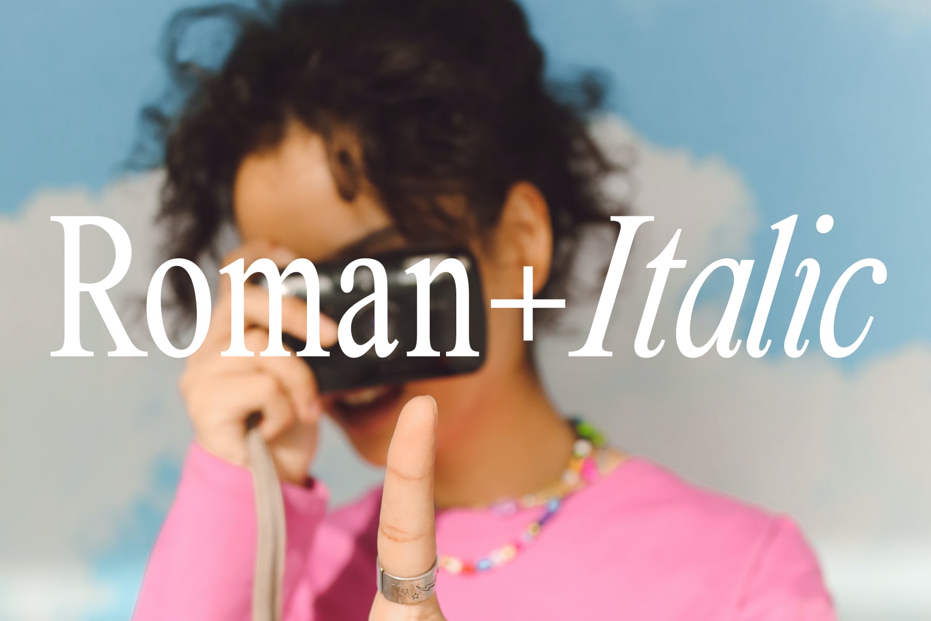 Woman in pink holding camera with Roman Italic font treatment across chest