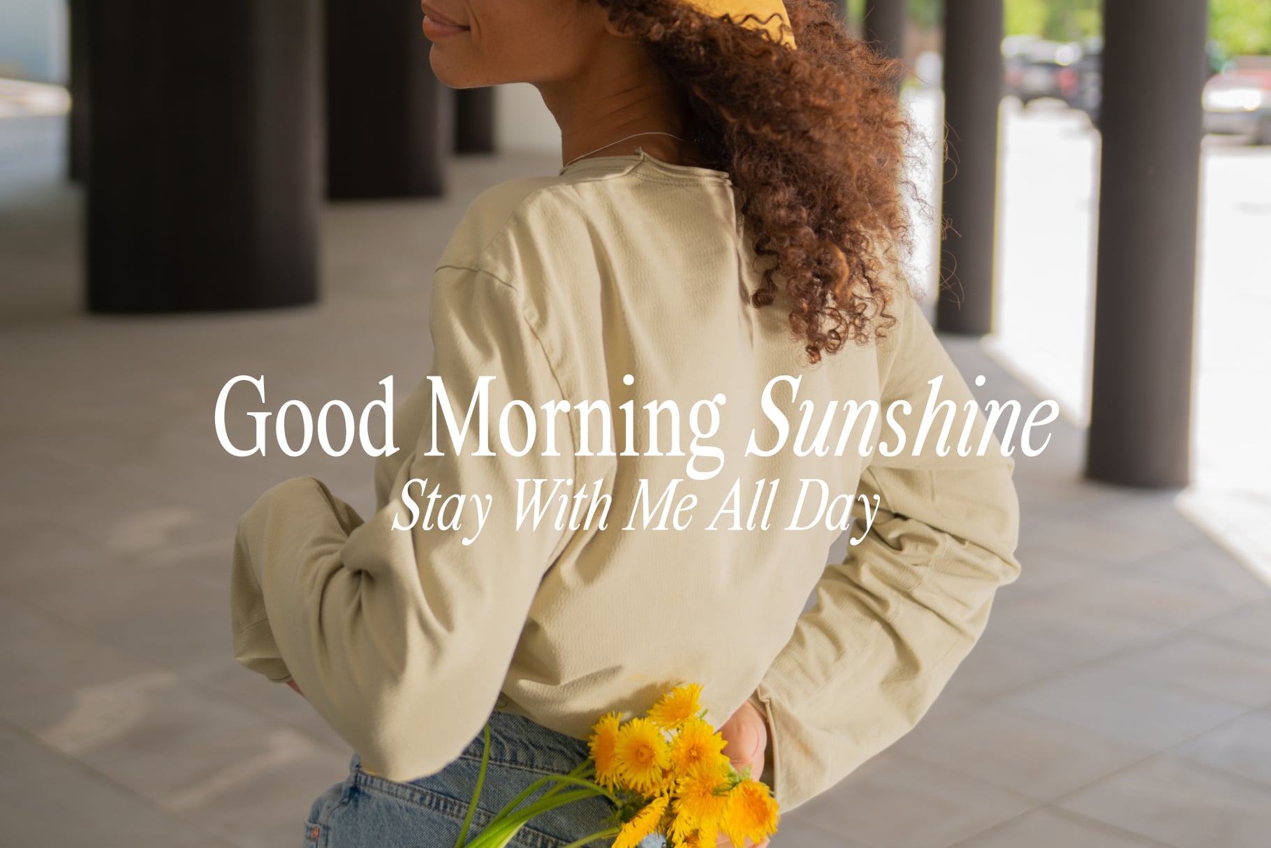 Woman from behind in cream jacket holding yellow flowers with Good Morning Sunshine overlay text