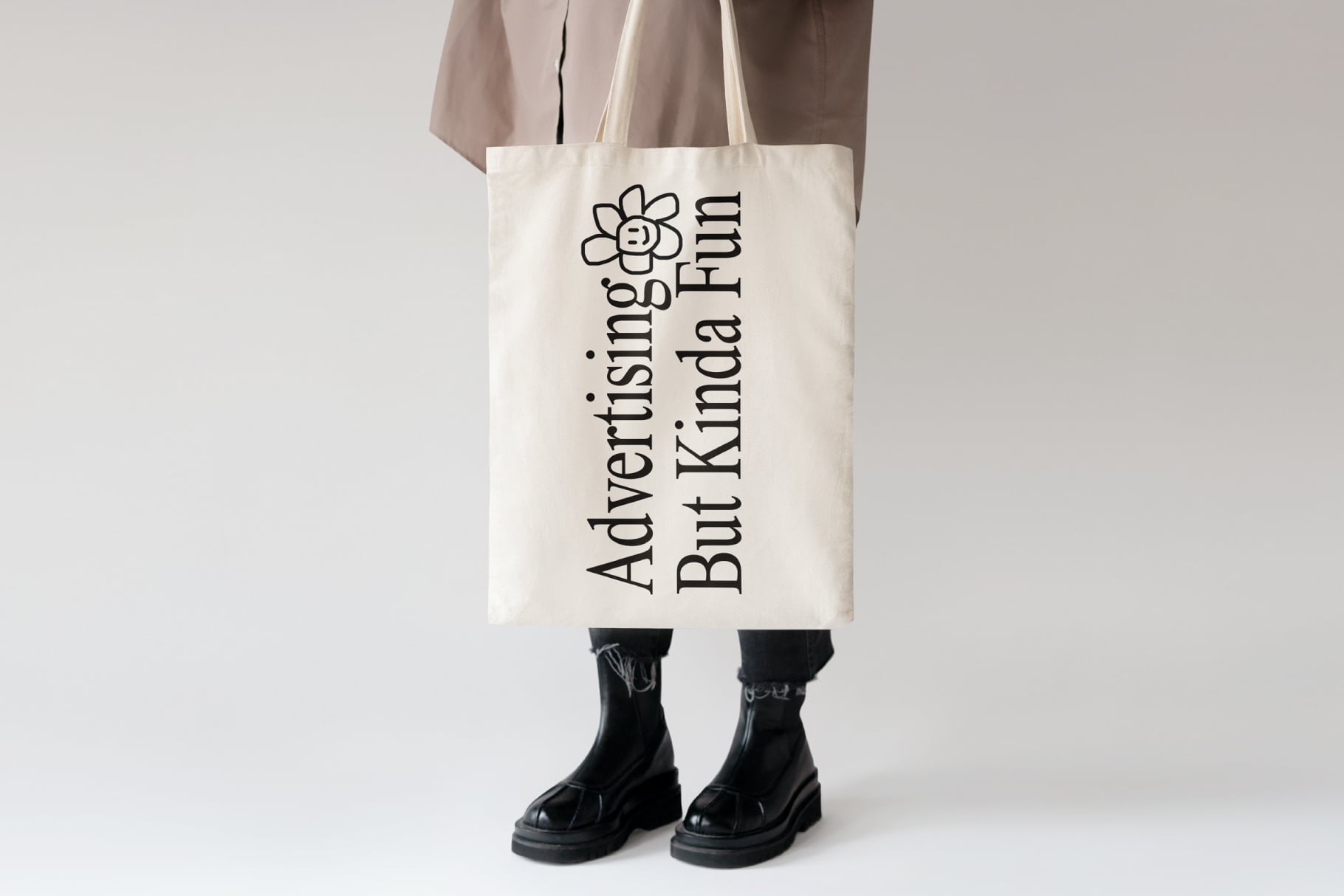 Canvas tote bag with Advertising But Kinda Fun text held by person in black platform boots