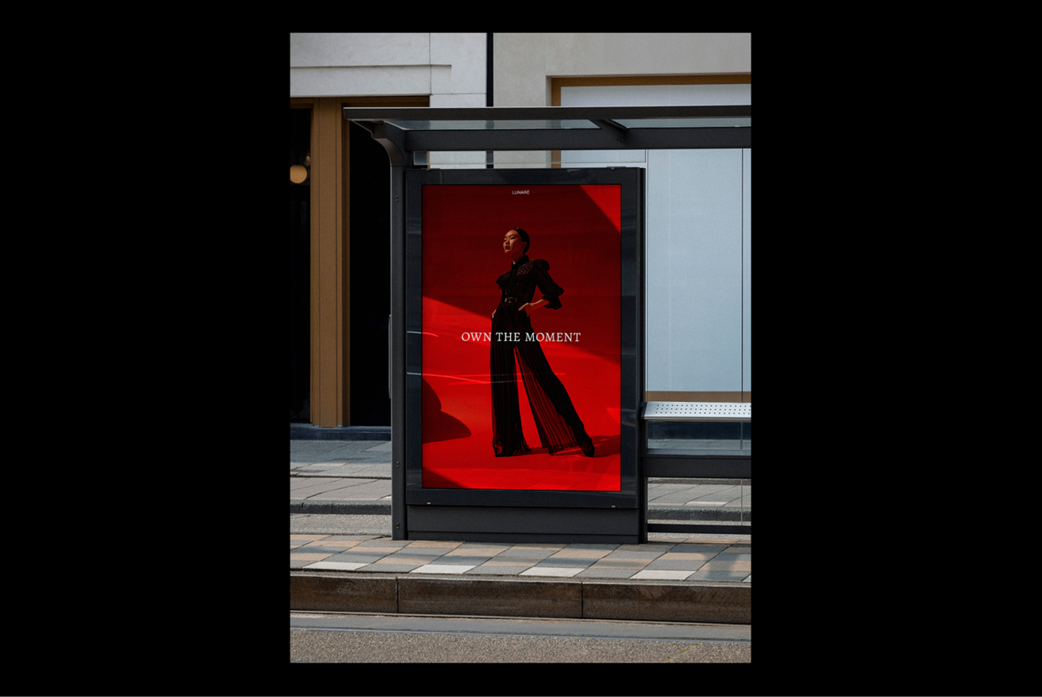Bus stop advertisement mockup featuring a model on a red background with text Own The Moment ideal for fashion and marketing design projects.
