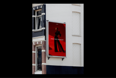Large urban billboard mockup on a building facade featuring a fashion ad with a model in black outfit and red background ideal for designers.