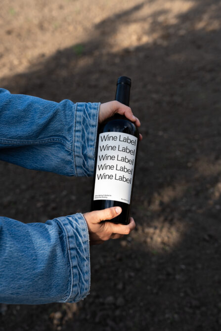 Bottle with white wine label mockup held in hand wearing denim jacket outdoors