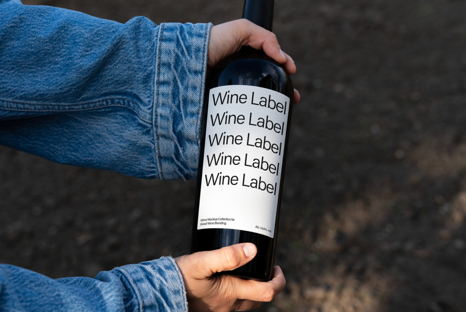Wine bottle mockup with white label in hands wearing denim sleeves, outdoor setting
