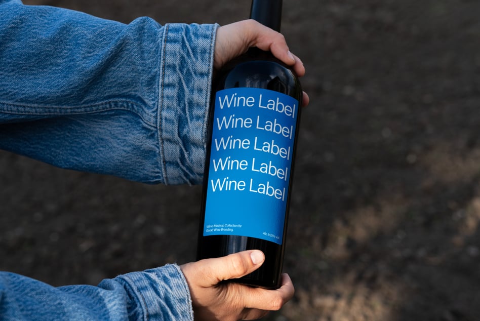 Wine bottle mockup with bright blue label held in hands against blurred ground background