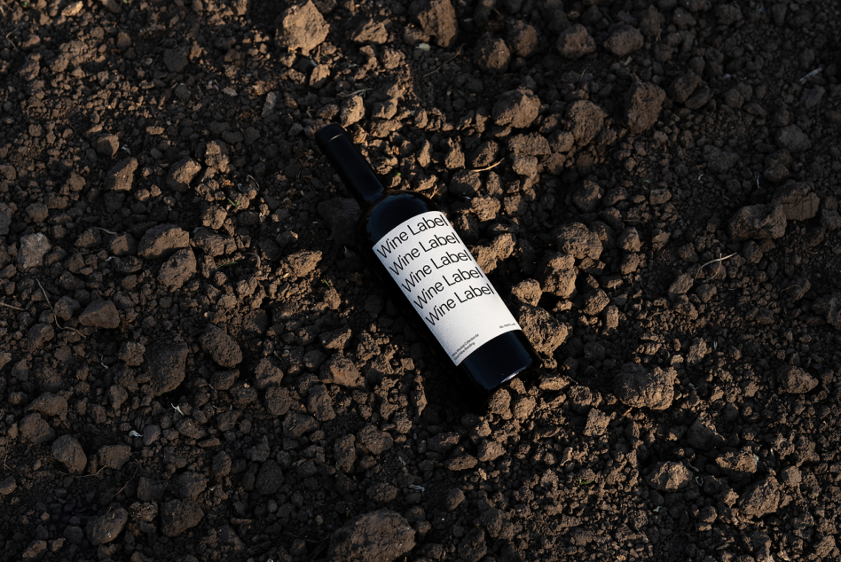 Wine bottle mockup with white label resting on textured ground surface overhead view