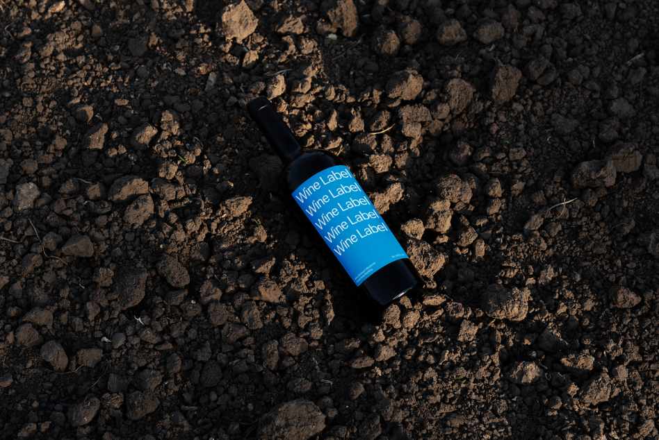 Wine bottle mockup with bright blue label placed on rocky terrain flat lay shot