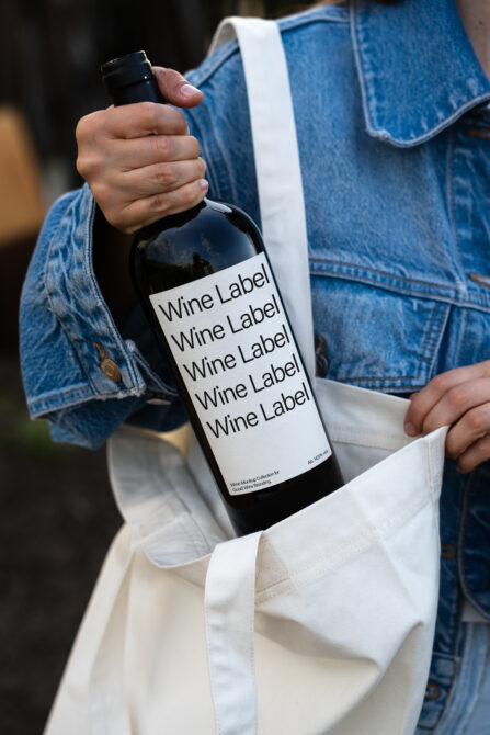 Wine bottle with white label mockup held in hands over denim jacket