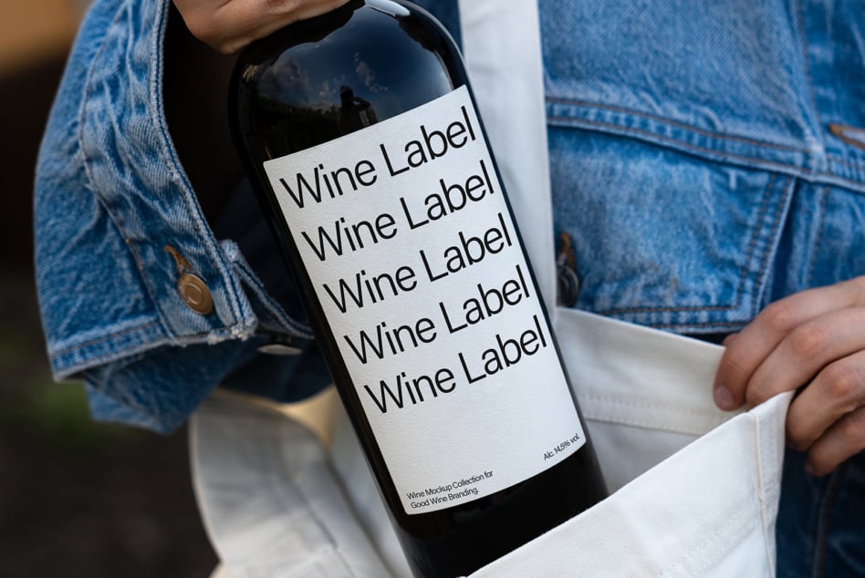 Wine bottle with cream label mockup in white bag held by person in denim