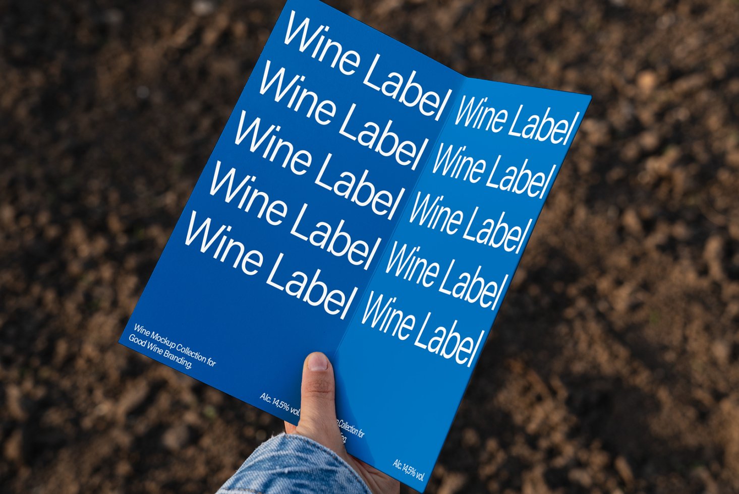 Person holds a blue folded wine label mockup card over a blurred earthy background. Ideal for branding design and templates. SEO keywords: mockup design brand.