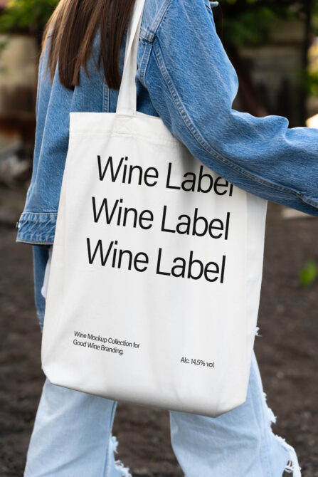 White tote bag with wine label mockup worn over shoulder in denim jacket