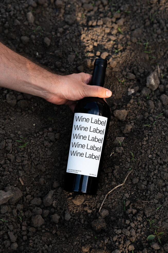 Hand holding wine bottle with mockup label in soil background wine design branding template graphic asset for designers mockup resource.