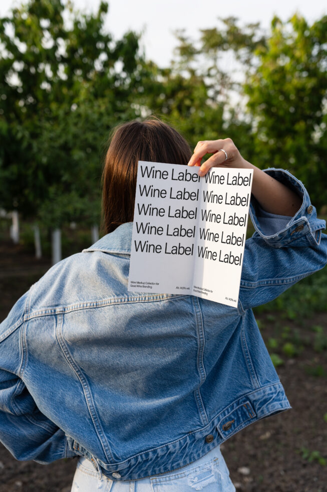Person outdoors holding a wine label mockup in hand. Ideal for designers seeking branding templates. Keywords: mockup, wine, label, design, template.