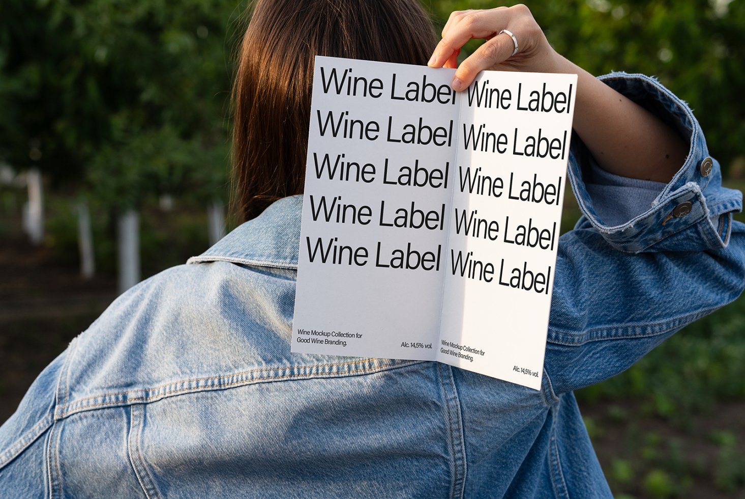 Designer holding a wine label mockup outdoors. The sheet shows repeated text Wine Label. Ideal for showcasing branding designs. Mockups for designers.