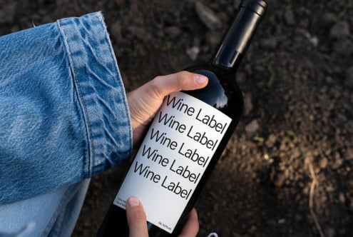 Hand holding wine bottle with white label mockup on dirt ground